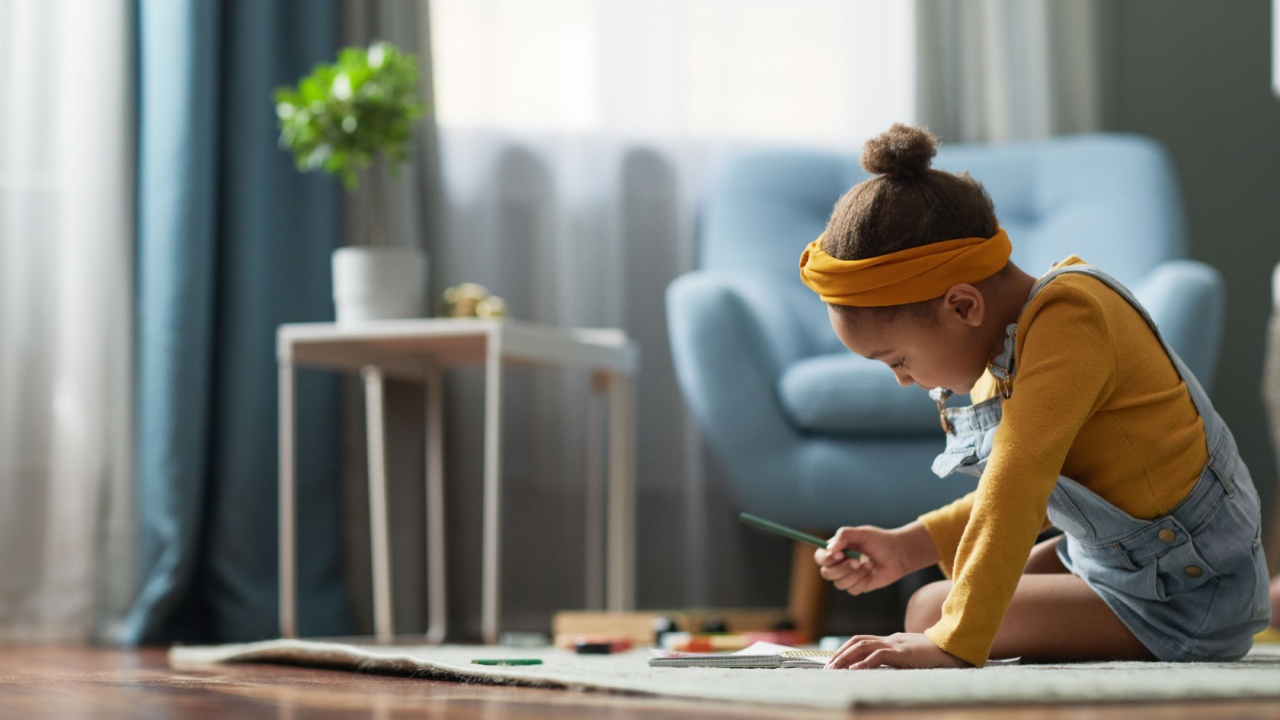 Side view portrait of cute African-American girl drawing while sitting on floor in cozy home interior, copy space