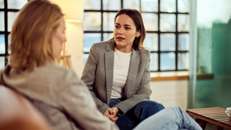 Two women engaged in a serious conversation in a brightly lit office.
