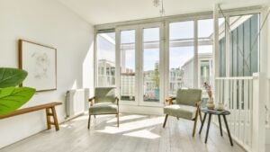 A serene and stylish indoor space featuring two elegant chairs, framed art, and abundant natural light streaming through large windows. Minimalist design enhances tranquility.