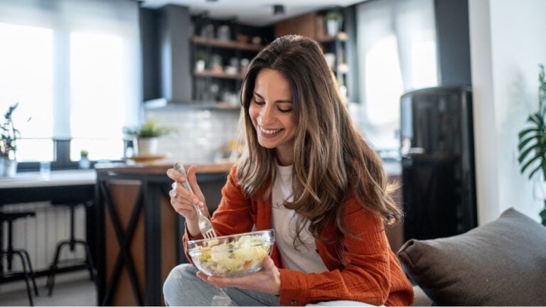 Smiling woman savoring a vibrant salad in a stylish, modern kitchen, celebrating a commitment to healthy eating and a balanced lifestyle filled with wellness and enjoyment