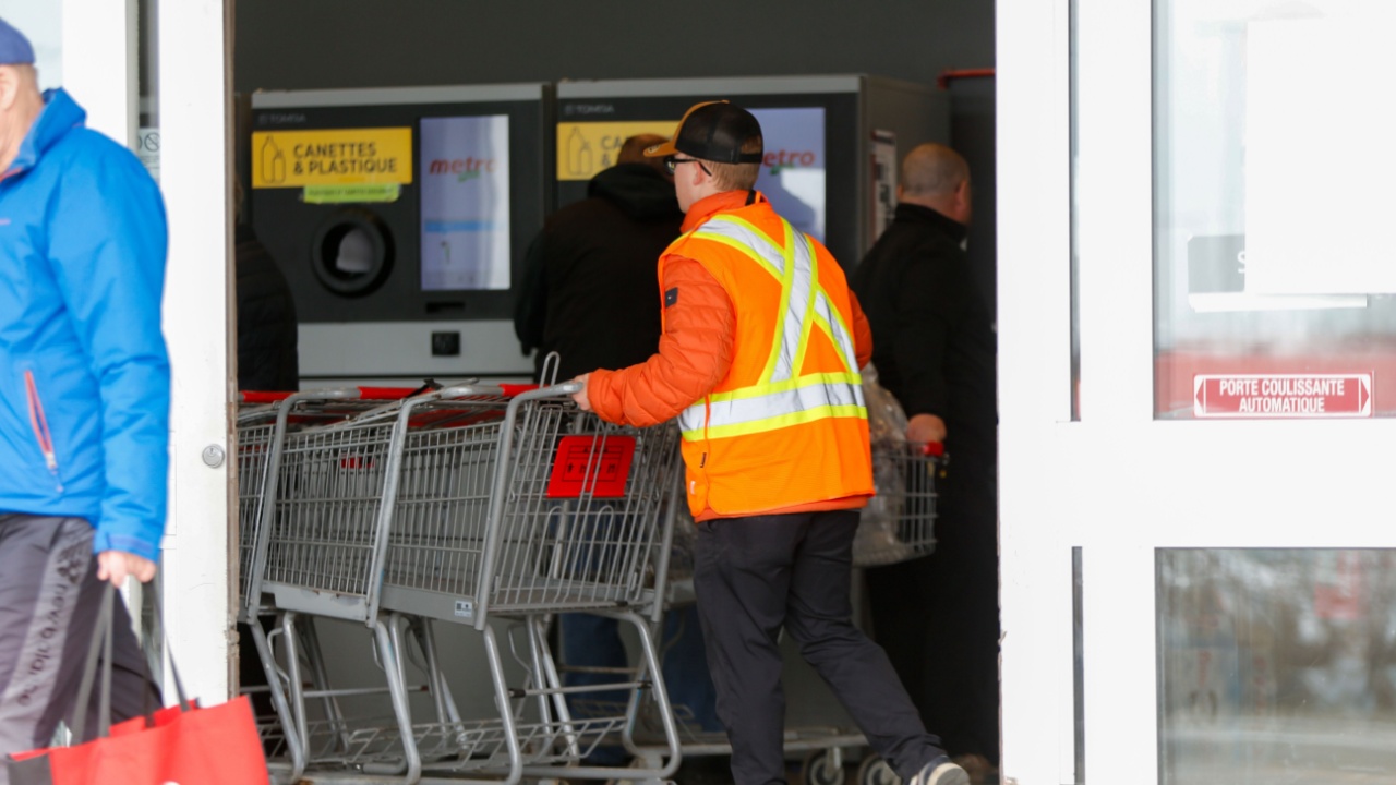 Quebec, Canada - 04-18-2025: A grocery store employee pushes baskets past the aluminum can recycling machines.