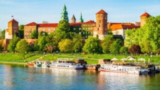 KRAKOW, POLAND - APR 23, 2025: View of Wawel castle and boats on bank of Vistula river in late aftenoon sunlight in spring season.