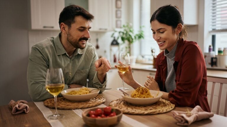 Happy couple communicating while eating pasta and drinking wine at dining table.
