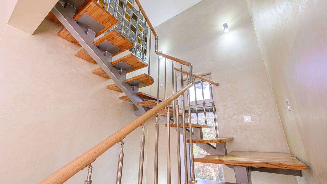 Elegant staircase with wooden steps, stainless steel railings, and textured walls. Light and airy space