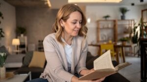 Smiling middle-aged woman enjoying reading a book while relaxing on a comfortable sofa in her modern living room, creating a cozy and peaceful atmosphere