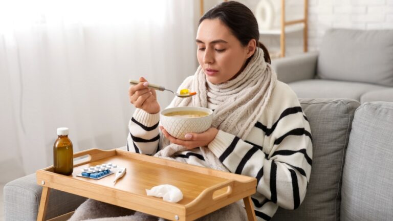 Sick young woman eating soup on sofa at home