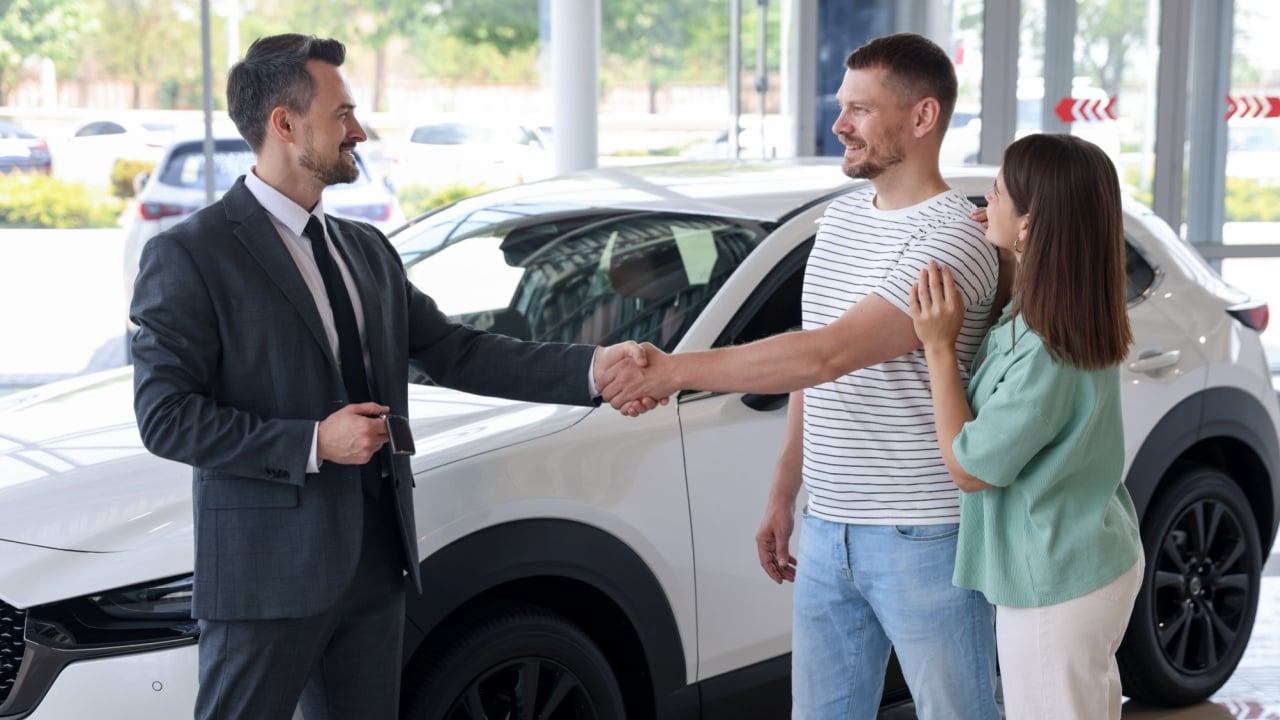 Salesman shaking hands with happy family near new car in salon