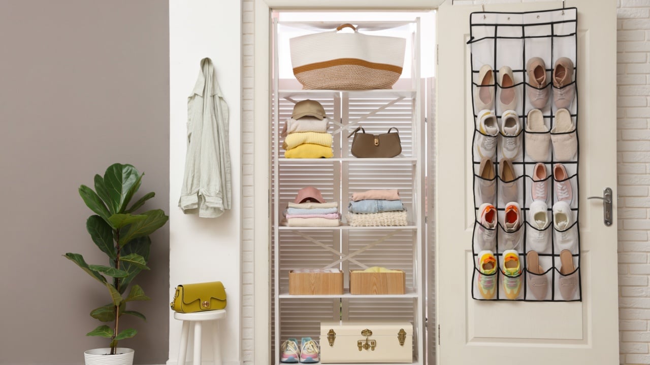 Organizer with different footwear on door, accessories and clothes indoors. Shoe storage