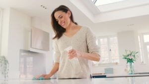 Woman At Home In Kitchen Doing Chores Wiping And Cleaning Surface With Antibacterial Spray Cleaner