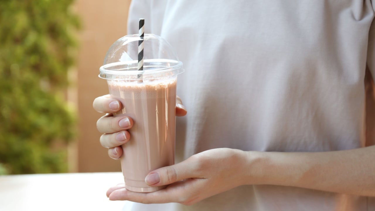 Woman holding tasty milkshake in plastic cup outdoors, closeup