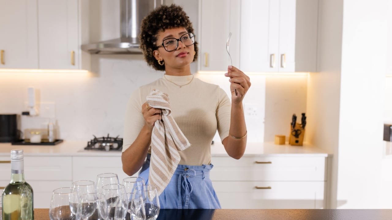 African American woman polishing cutlery in modern kitchen, preparing for event. Hospitality, preparation, catering, utensils, domestic, professional