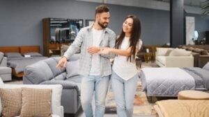 Joyful couple actively choosing new sofa or bed, pointing and discussing details in a furniture store showroom