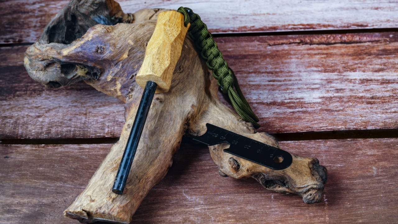 Ferrocerium rod with wooden handle, striker, and paracord lanyard lying on a piece of wood and a wooden background, ready for fire starting