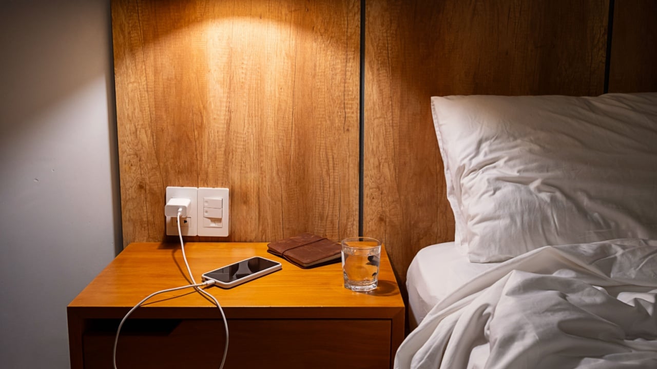 Mobile phone charging on bedside table in comfortable hotel or home bedroom. Modern living and relaxation.