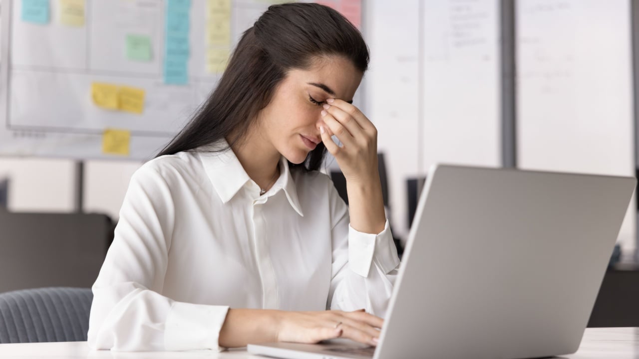 Too much screen time. Tired fatigued young female office worker sit at desk by notebook with closed eyes rub nose bridge suffer from migraine eye strain tension headache stressed with mental burnout