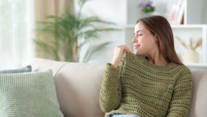 Satisfied woman in green smelling sweater sitting in a sofa at home