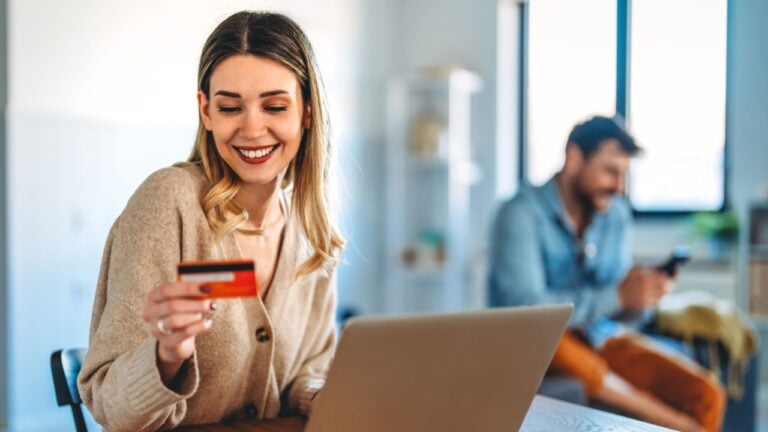 Smiling woman holding a credit card and shopping online at home with a laptop, online purchase
