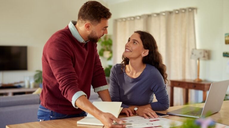 Young positive couple working together at home with financial documents and bills. Man and woman planning on yearly budget for financial home, savings concept. Middle aged couple checking energy consumption bills at home while working together on laptop.