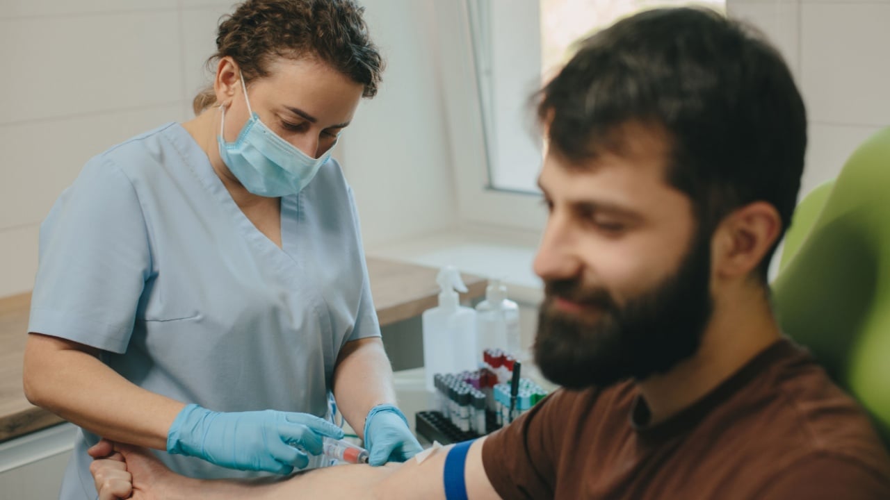 Medical professional performing blood collection procedure on male patient's arm in clinic. Healthcare and diagnostic concept
