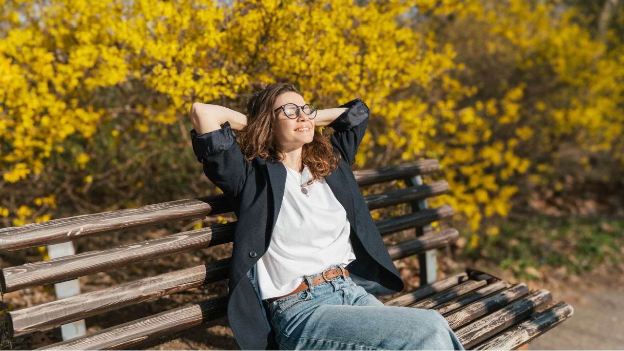 Relaxed young curly woman in glasses enjoying spring sun on a city bench