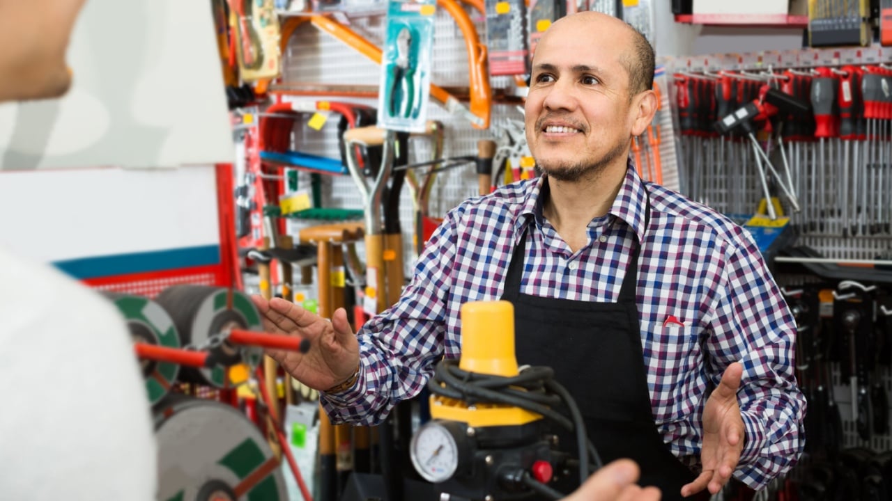 happy American mature seller showing customer electric compressor in household store