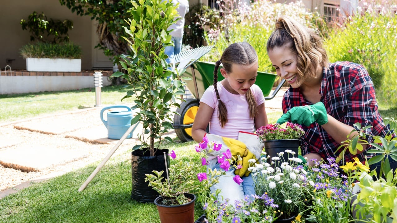 Smiling mother and daughter gardening together in garden on a sunny day
