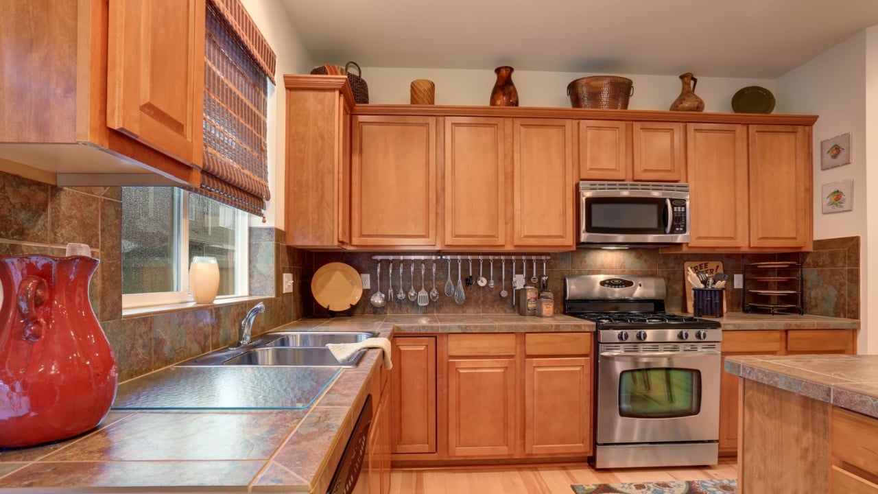 View of kitchen with hardwood storage combination, steel appliances and tile counter tops.