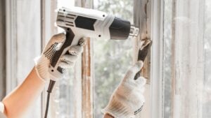 Master removes old paint from window with heat gun and scraper. Closeup