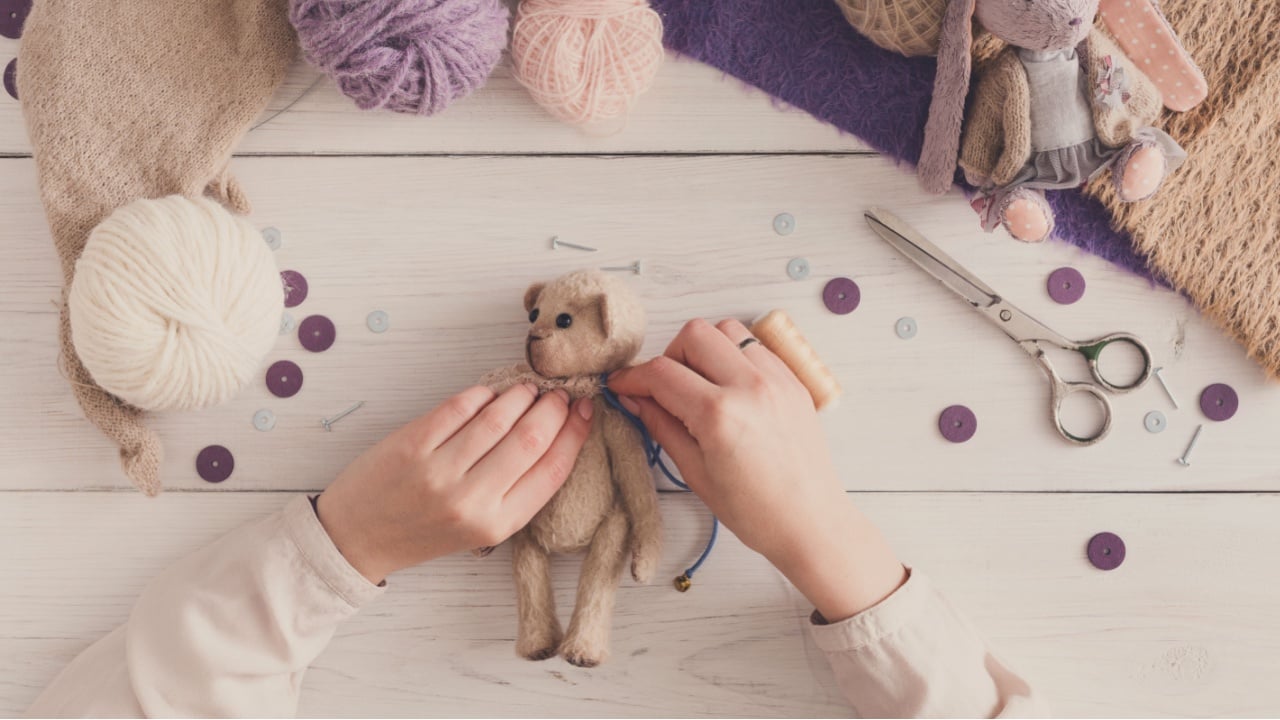 Process of making vintage toy, top view. Artisan pov, needlewoman hands sewing handmade teddy bear, home workshop