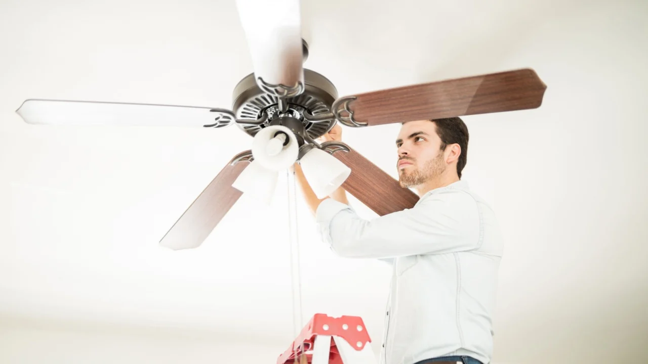 Portrait of a busy handyman standing on a ladder and fixing a ceiling fan in a house