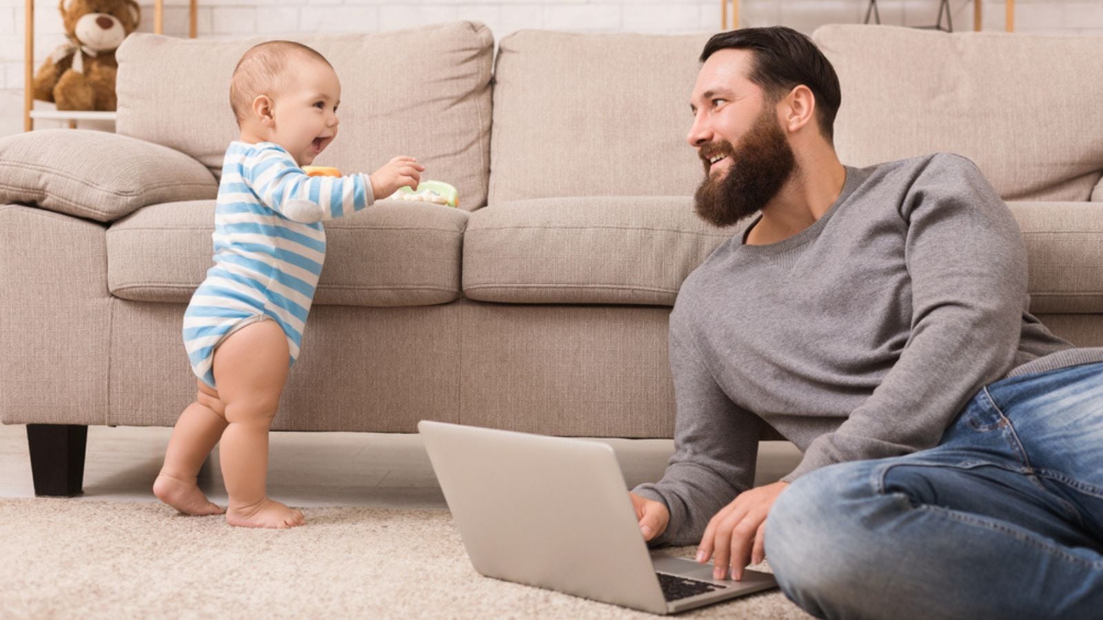 Young dad working on laptop and taking care of his baby son