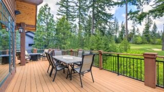 Beautiful large cabin home with large wooden deck and chairs with table overlooking golf course.