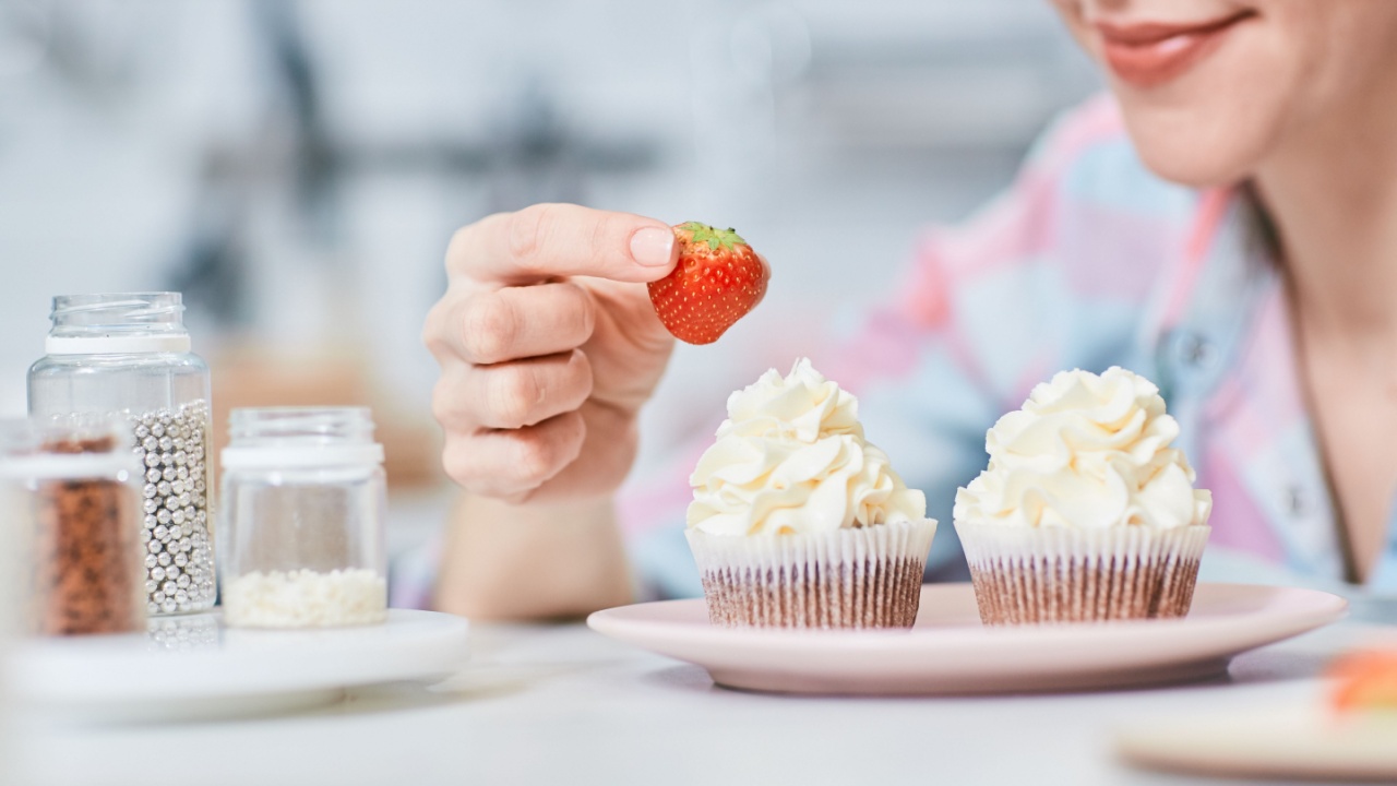 Woman putting appetizing fresh strawberry on creamy topping of cupcake