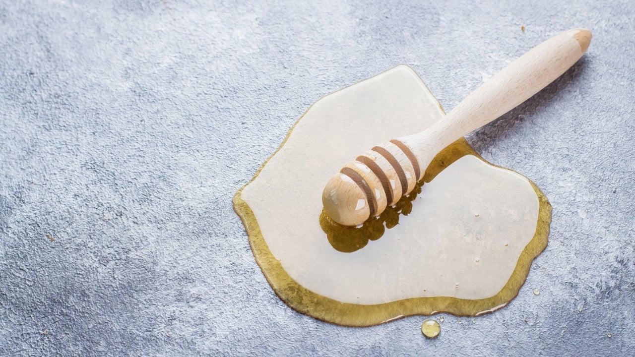 Wooden dipper in a spilled honey over gray stone table background