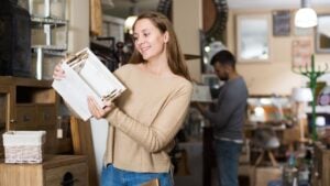 Young woman looking for stylish knickknacks for apartment in shop of secondhand furniture