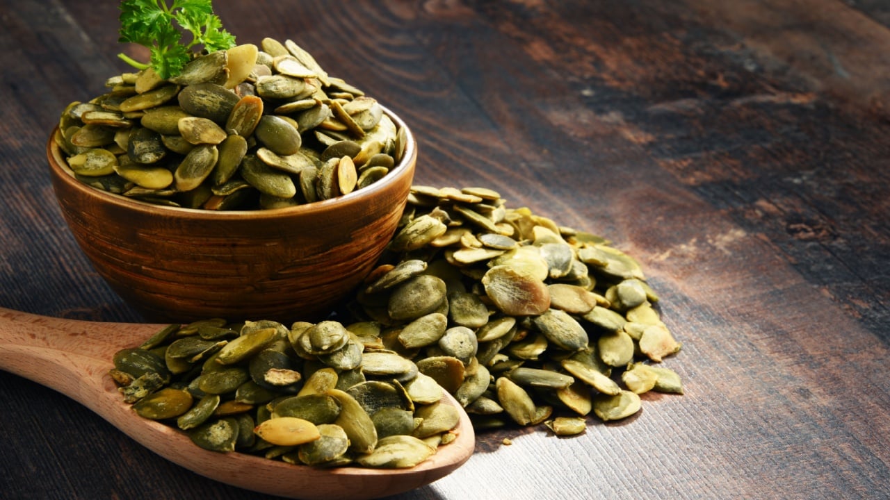 Composition with bowl of pumpkin seeds on wooden table.
