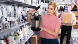 smiling housewife choosing new modern juicer for kitchen in furniture shop