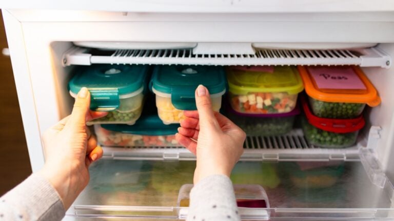 Woman taking containers with frozen peas and corn out from freezer.
