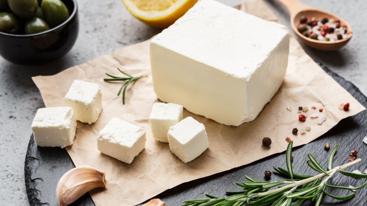 Block of feta cheese, olives, herbs and spicies on board over concrete background. Traditional greek food concept