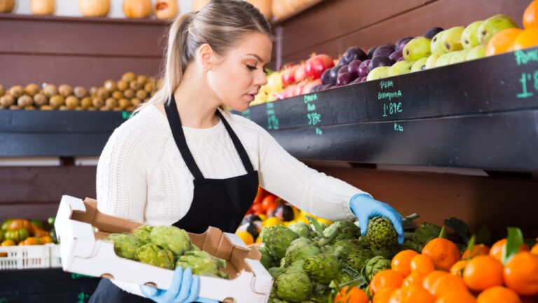 Young woman grocery worker arranging fruits on store shelves