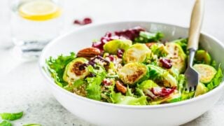 Fried brussels sprouts salad with quinoa, cranberries and nuts in a white bowl.