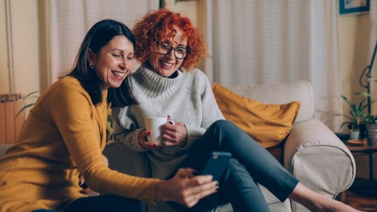 middle aged female friends having fun at home, using mobile phone