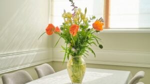 Bouquet of spring summer flowers and red poppies in vase, standing on table in living room, dining area near window
