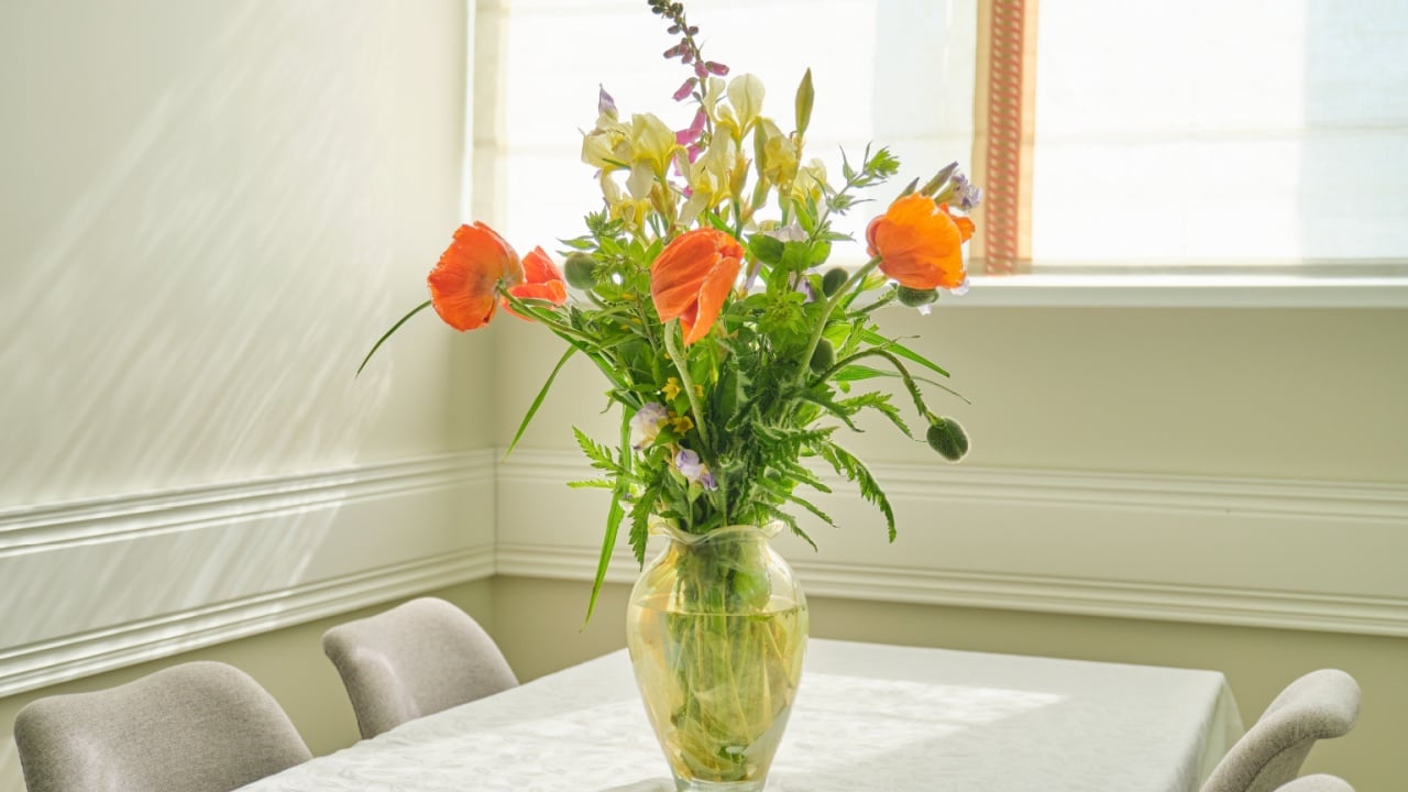Bouquet of spring summer flowers and red poppies in vase, standing on table in living room, dining area near window