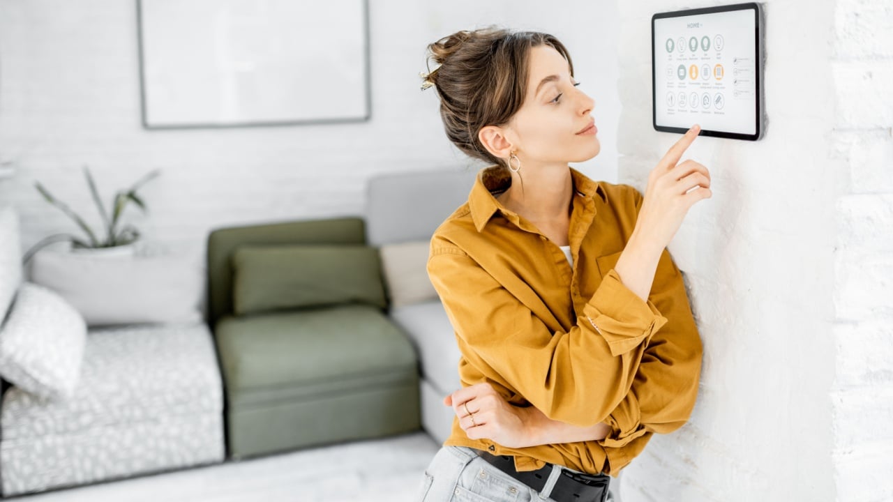 Woman controlling home with a digital touch screen panel installed on the wall in the living room