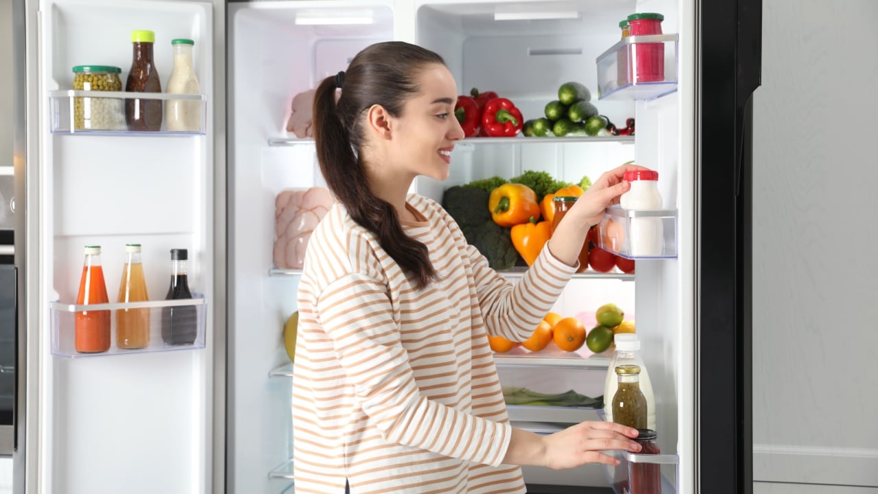 Young woman taking yoghurt out of refrigerator indoors