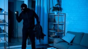 Robbery Concept. Disguised burglar standing in apartment or office, using flashlight, searching something to steal