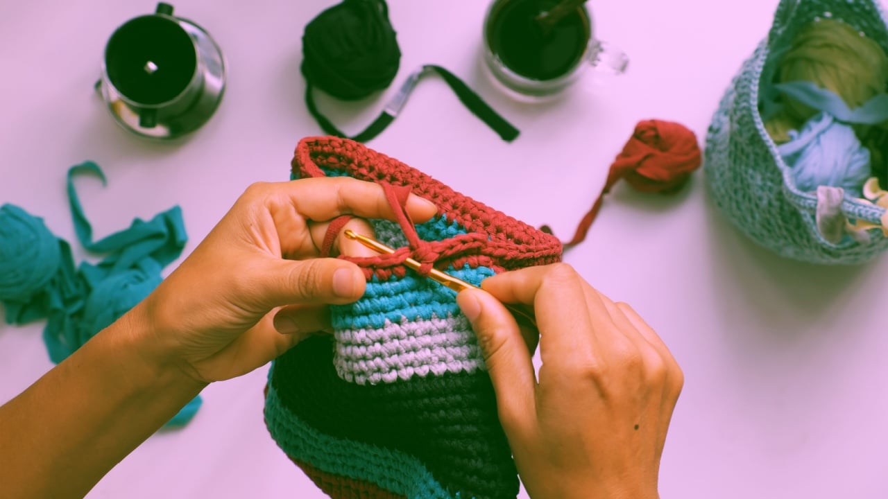 Close up from top view woman hand hold colorful handmade bag from recycle old t shirt on white background, reuse clothes by cut in yarns then crochet to make diy product in leisure activity
