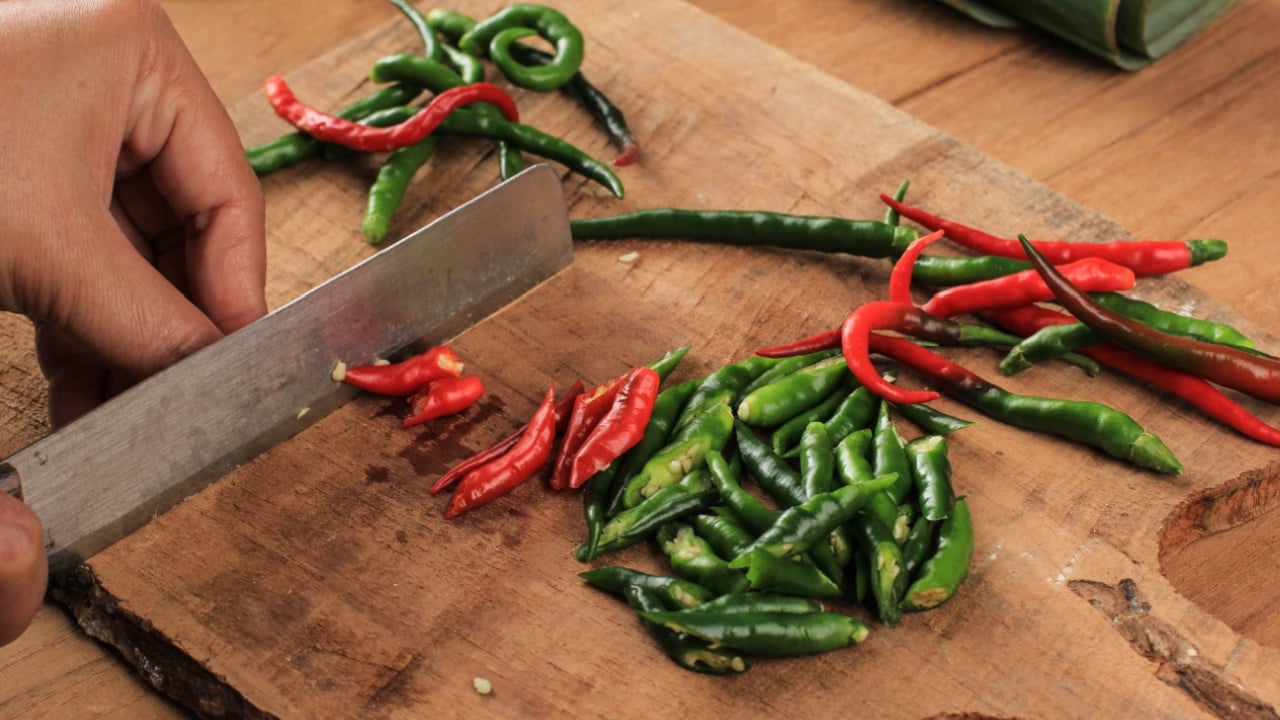Female Hand Slicing Cut Chilli Pepper on Wooden Chopping Board Using Knife