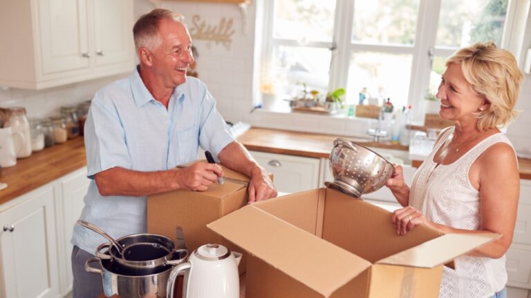 Senior Couple Downsizing In Retirement Packing And Labelling Boxes Ready For Move Into New Home